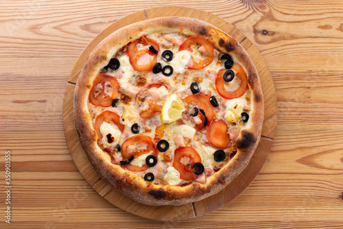hearty italian pizza on a wooden board. pizza with seafood, cheese, tomatoes and olives and a slice of lemon
