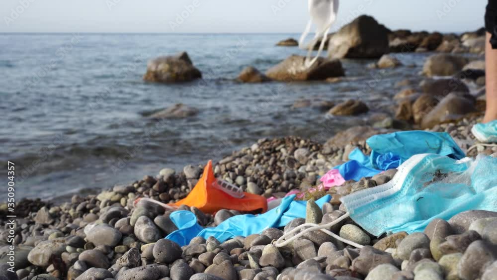 COVID-19 plastic waste: Used medical masks and latex gloves washed up to the beach. Garbage collector cleans the seashore. Environmental and ocean pollution during Coronavirus pandemic COVID-19 plastic waste: Used medical masks and latex gloves washed up to the beach. Garbage collector cleans the seashore. Environmental and ocean pollution during Coronavirus pandemic