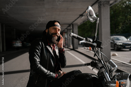 Call for friends in roaming. Biker traveller, brutal bearded man street racer sitting oh his motorcycle bike and talking phone. People lifestyle and hobby. 