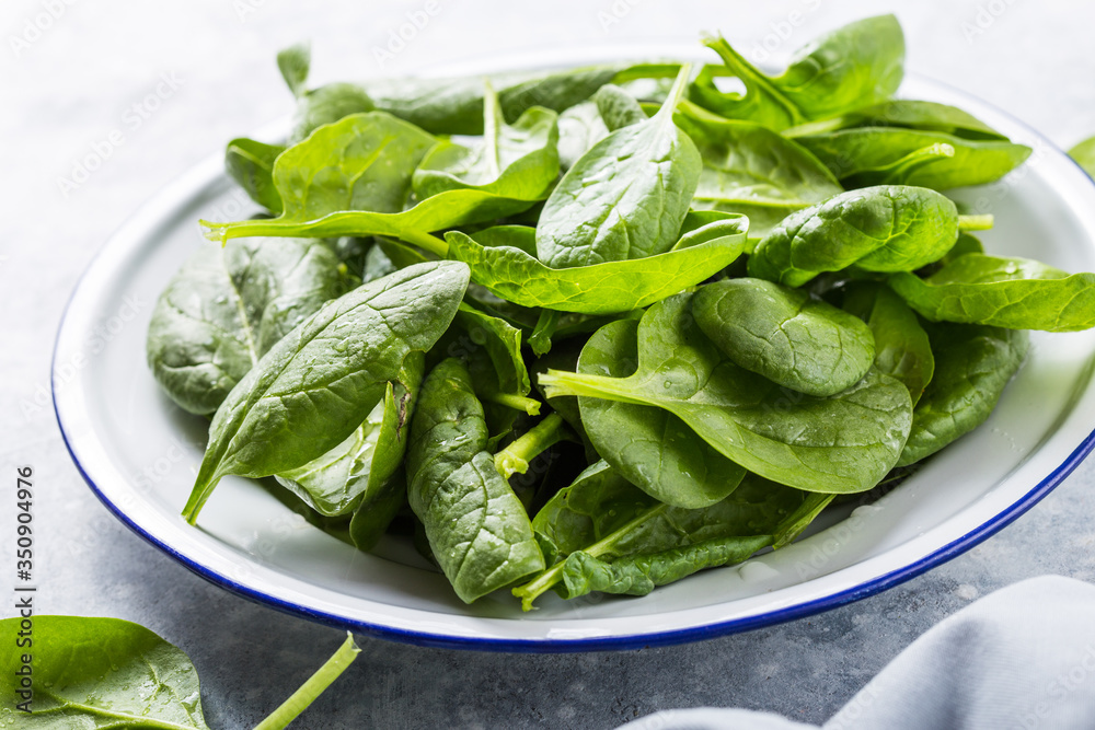 Fototapeta premium Baby spinach leaves in bowl on grey concrete background, top view, copy space. Clean eating, detox, diet food ingredient