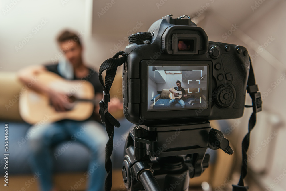 Naklejka premium selective focus of young vlogger playing guitar while looking at digital camera