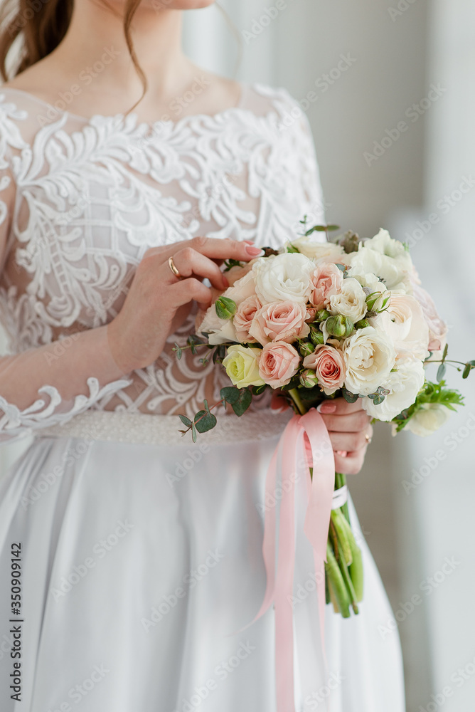The wedding bouquet in the hands of the bride. The bride holds the bouquet. The wedding bouquet with ribbons. 