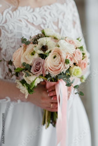 The wedding bouquet in the hands of the bride. The bride holds the bouquet. The wedding bouquet with ribbons. 