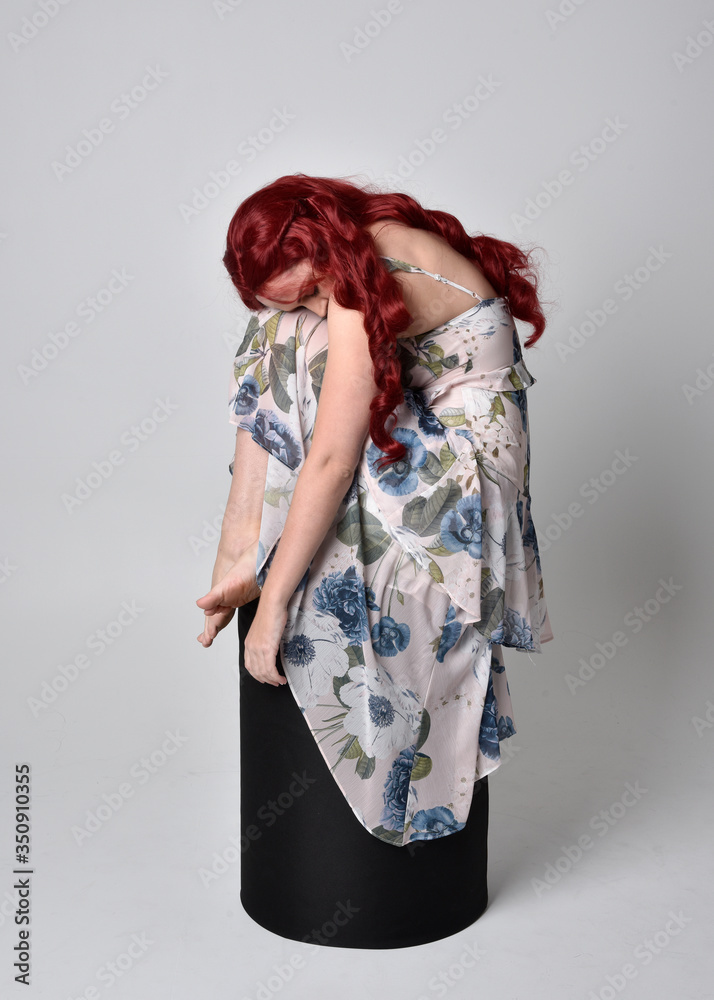 Portrait of a beautiful woman with red hair wearing a flowing floral gown. full length standing pose, isolated against a studio background Portrait of a beautiful woman with red hair wearing a flowing floral gown. full length standing pose, isolated against a studio background