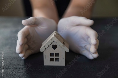 ..girl is holding the wooden house with her gloved hands. stay at home . covit -19