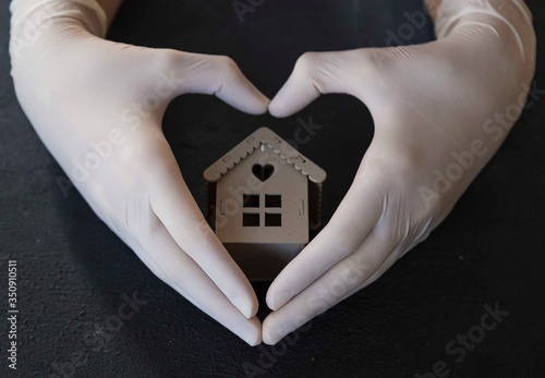 ..girl is holding the wooden house with her gloved hands. stay at home . covit -19