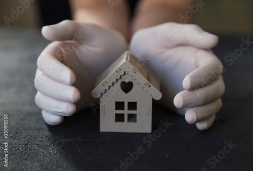 ..girl is holding the wooden house with her gloved hands. stay at home . covit -19
