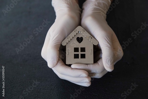 ..girl is holding the wooden house with her gloved hands. stay at home . covit -19