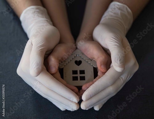..girl is holding the wooden house with her gloved hands. stay at home . covit -19
