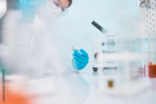 Female lab technician in safety glasses with pipette  blurred background.