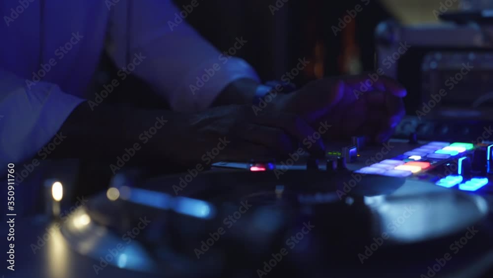 A close up detail shot of a Dj adjusting the volume levels on a mixer in a night club