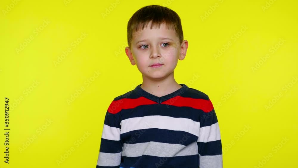 Serious little child smiles on a yellow background with copy space. Little boy in a colorful sweater. Place for text or product. 4K slowmotion footage Serious little child smiles on a yellow background with copy space. Little boy in a colorful sweater. Place for text or product. 4K slowmotion footage