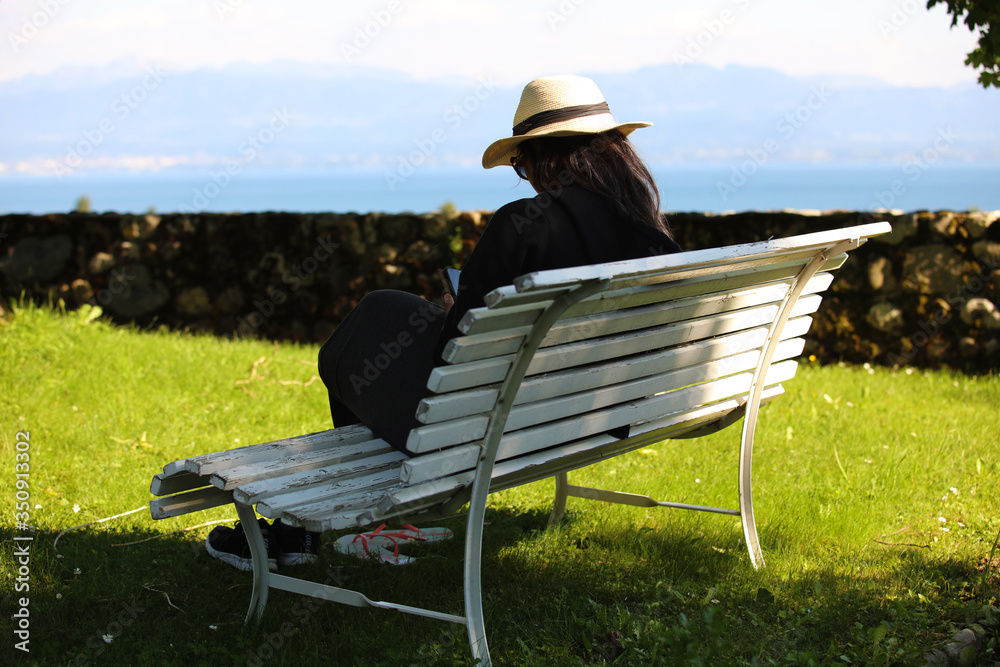 A woman with a hat uses her smartphone on a white bench