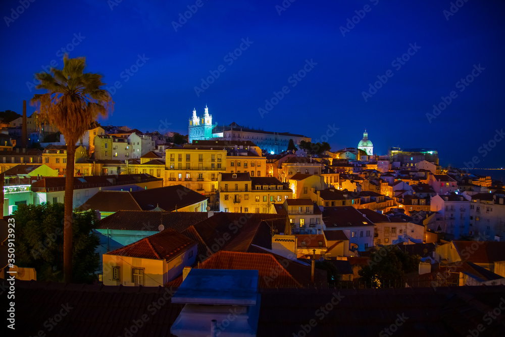 Night view of Alfama district and Santo Estevao church seen from Miradouro das Portas do Sol view point in Lisbon, Portugal