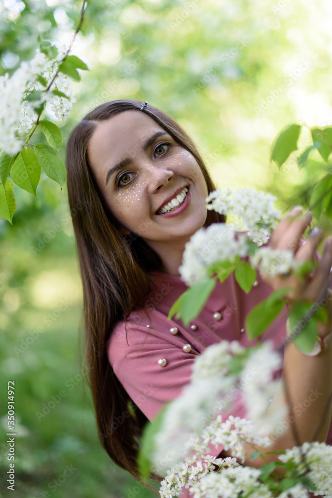 Portrait of happy girl in a pink t shirt holding flowering cherry branch and looking at the camera in sunny spring day in park Portrait of happy girl in a pink t shirt holding flowering cherry branch and looking at the camera in sunny spring day in park