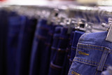 Blurred background with rows of jeans, clothes on hangers out of focus. The photo