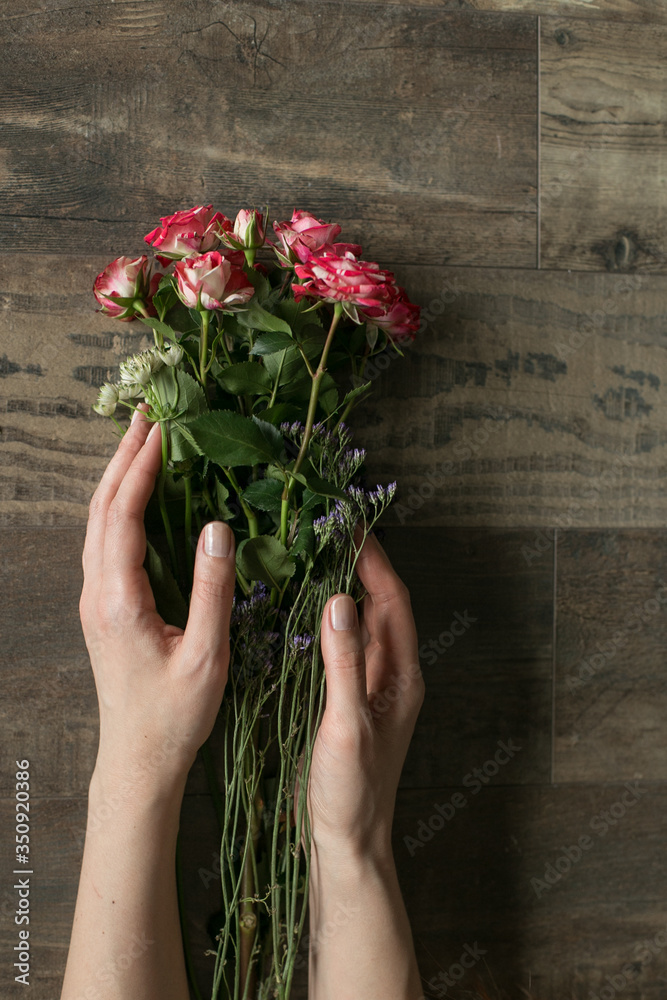 Woman's hand with good manicure with flowers at the floor.. Wooden floor with bouquet. Present at the date. Image with selective focus.