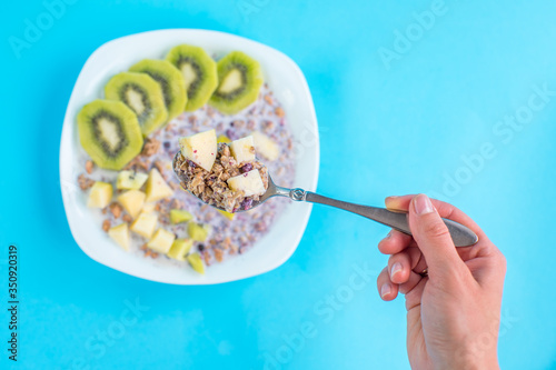 woman eating muesli with kiwi and apple with milk on a blue background close up. healthy food. many nutrients.