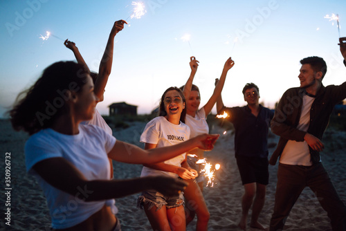 Group of friends at night on the beach with sparklers. Young friends enjoying on beach holiday. Summer holidays, vacation, relax and lifestyle concept.