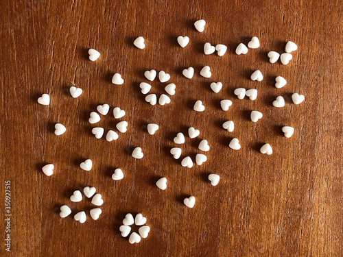 White pills in the shape of a heart scattered on a wooden background. Coronavirus concept.