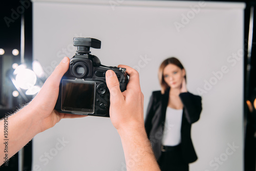 Selective focus of photographer holding digital camera near model in photo studio
