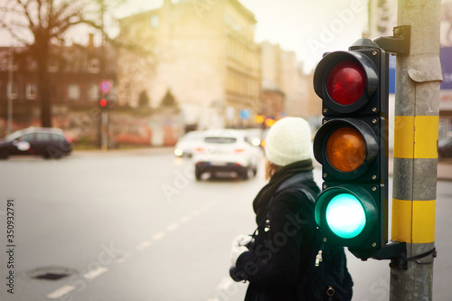 Green traffic light on a city street. A woman is waiting at a pedestrian crossing.