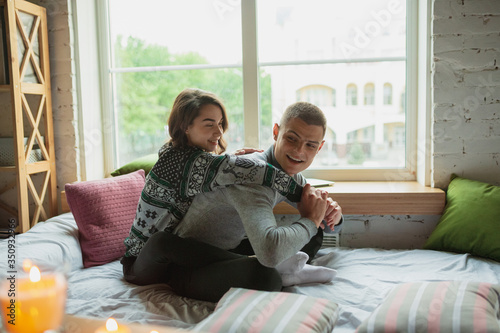Pillows fight, having fun. Quarantine lockdown, stay home concept - young beautiful couple enjoying new lifestyle during coronavirus worldwide health emergency. Happiness, togetherness, healthcare.