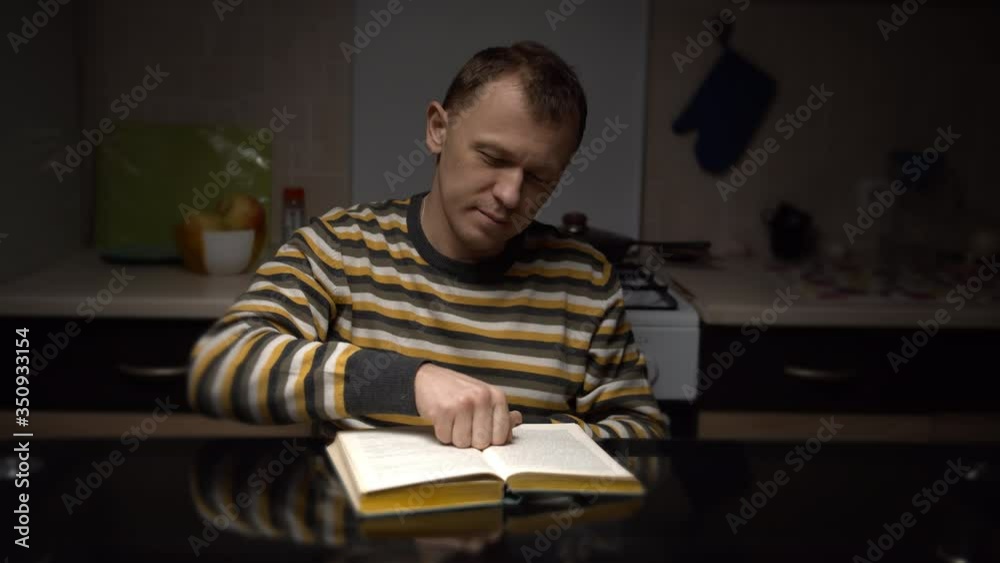 A man sits at a table late at night and reads a book A man sits at a table late at night and reads a book