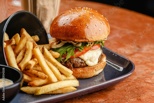 
Burger with beef and cheese on a plate with french fries, side view. Board with tasty burger, french fries and vegetables on wooden table. tray with delicious burger and french fries.
