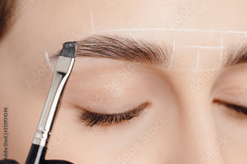 Correction and tint of eyebrows, master applies brush to woman marking on brow
