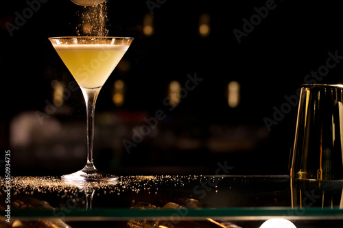 Valokuva dropping sugar onto a ginger cocktail, yellow cocktail ob a table, on dark background