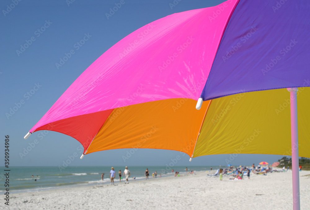 colorful umbrella on beach, cropped close, with beach scene in the background