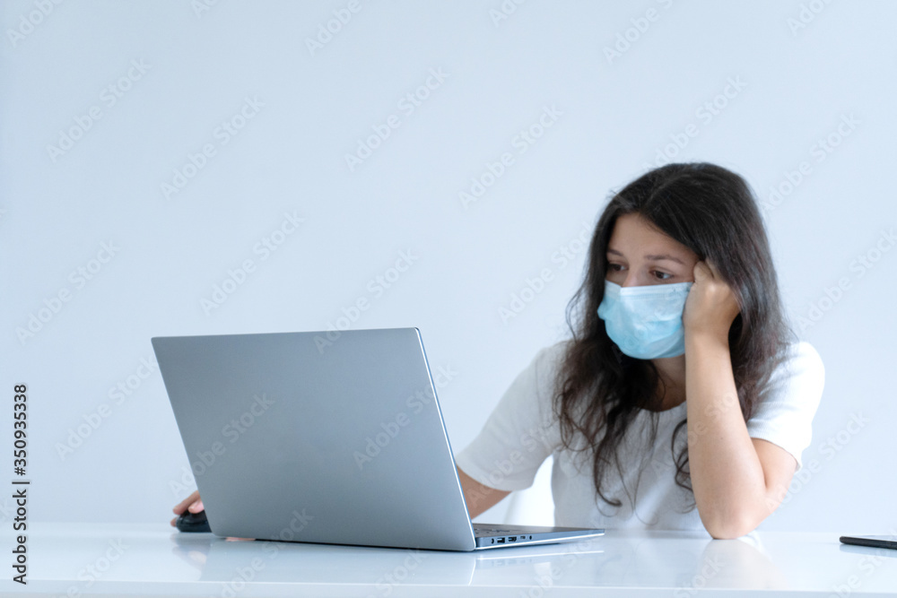 The girl works from home during quarantine. Corona virus pandemic. A girl in a surgical mask works on a laptop and drinks coffee. Distant work The girl works from home during quarantine. Corona virus pandemic. A girl in a surgical mask works on a laptop and drinks coffee. Distant work