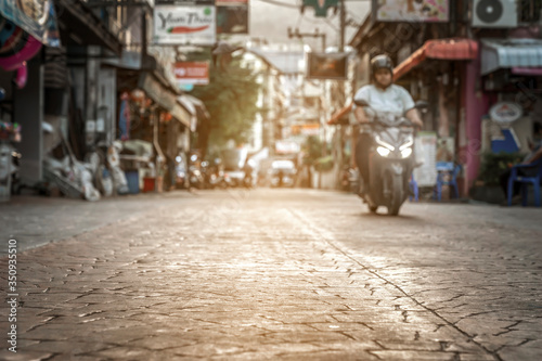 blurred background - a quiet calm deserted city street in Asia in Thailand at sunset in the evening. passing moped bike. Sunlight on the sidewalk, romantic cozy atmosphere © Vladimir Razgulyaev