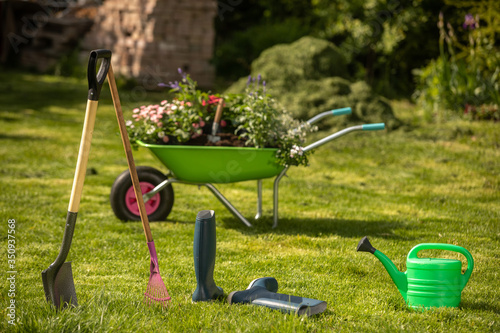 Wheelbarrow with gardening tools in the garden. Rakes, shovel, pitchfork, watering can. Beautiful background for the gardening concept