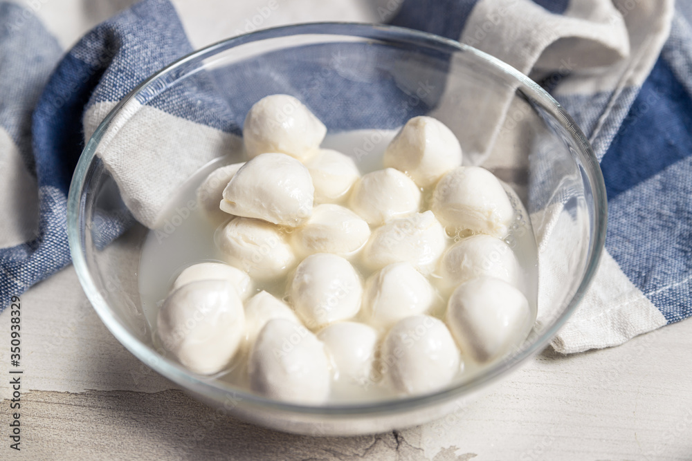 Small mozzarella balls in brine in a transparent bowl next to a blue towel Small mozzarella balls in brine in a transparent bowl next to a blue towel