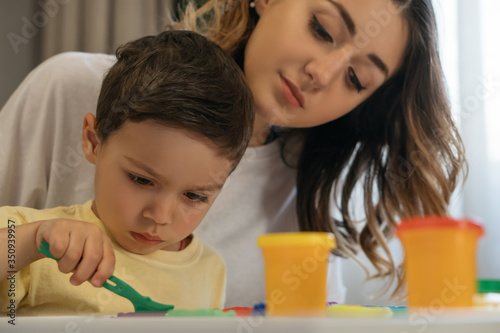 young mother looking at concentrated son holding spatula near plasticine