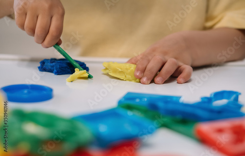 cropped view of little boy cutting colorful plasticine with spatula