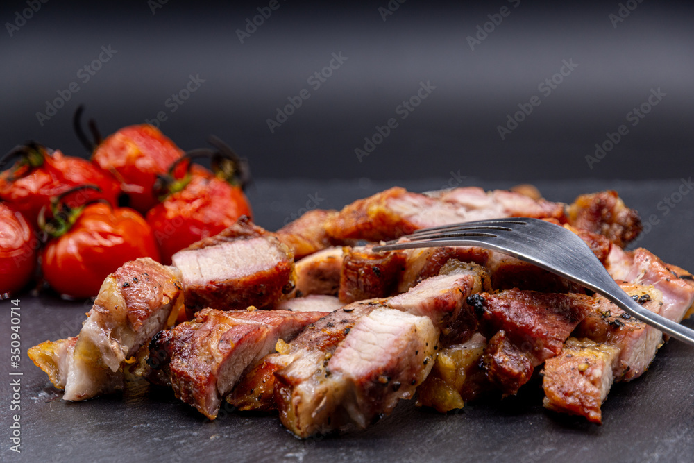 pork steak on black slate and grilled tomatoes ans salt