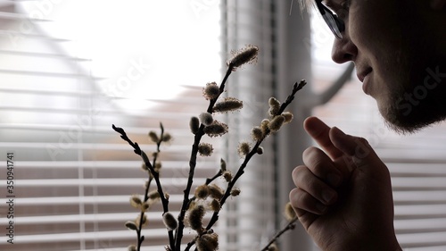 young man in glasses sniffing a houseplant