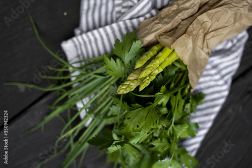 parsley onion and asparagus in a craft bag on a dark wooden blurred background