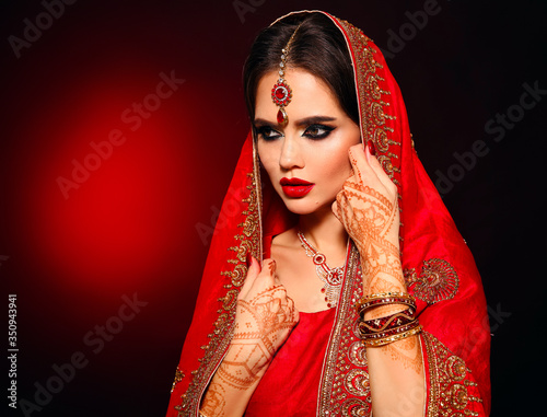 Portrait of beautiful indian girl in red bridal sari. Young hindu woman model with kundan jewelry set. Traditional Indian costume lehenga choli. Henna painting, mehendi on bride's hands.