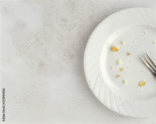 Soft focus empty white plate with crumbs and fork against marble