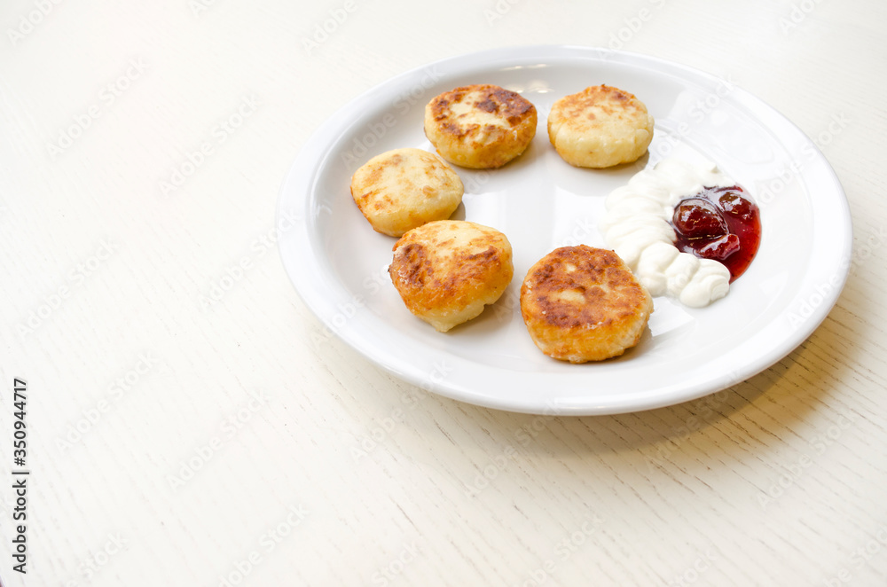 Cheese pancakes on the plate, top view. Fried cheesecakes served with sour cream and jam. Delicious homemade dish with copy space.