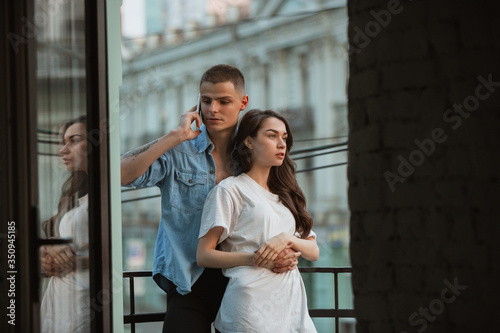 On the balcony, lovely. Quarantine lockdown, stay home concept - young beautiful caucasian couple enjoying new lifestyle during coronavirus health emergency. Happiness, togetherness, healthcare.