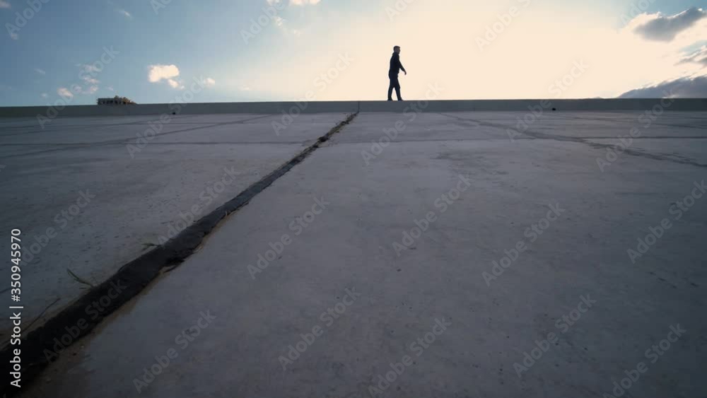A man walks into the distance, his face is not visible. In the foreground are concrete slabs. The frame is dynamic, shot through the passage. Sunny summer day on the street. A man walks into the distance, his face is not visible. In the foreground are concrete slabs. The frame is dynamic, shot through the passage. Sunny summer day on the street.