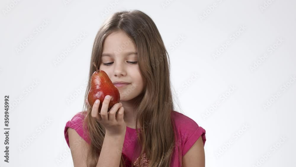 A little girl on a white background holds in his hand a ripe fragrant pear. The girl bites and eats a delicious red pear. A little girl on a white background holds in his hand a ripe fragrant pear. The girl bites and eats a delicious red pear.