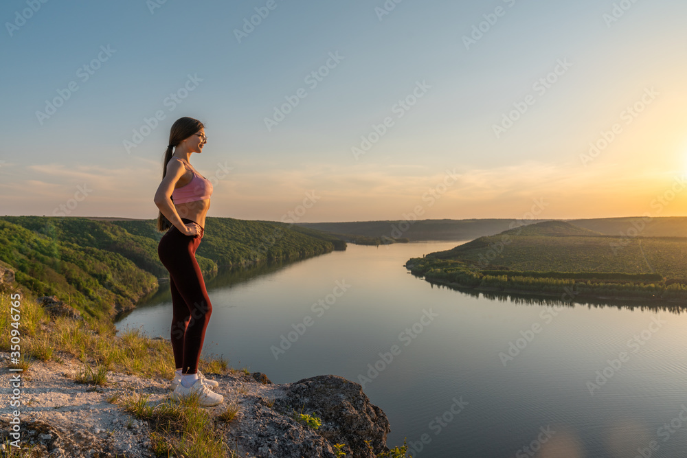 Young active hiker woman in sportswear and glasses relaxing on a rock at high altitude, watching beautiful panorama with sunset Young active hiker woman in sportswear and glasses relaxing on a rock at high altitude, watching beautiful panorama with sunset