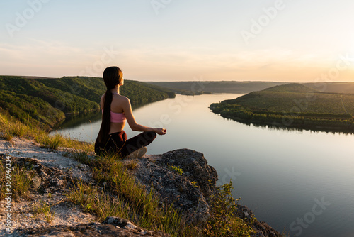 Brunette woman practicing yoga and sitting in lotus pose outdoor with amazing river view.