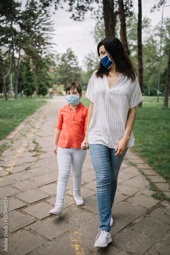 Mom and child walking on park alley while wearing antivirus masks. Woman holding little girl's hand while walking in park and wearing medical masks against coronavirus. © Synergic Works OÜ